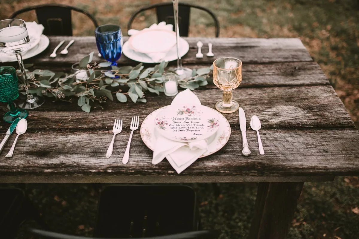 Table en bois avec runner d'eucalyptus, vaisselle vintage et verres colorés pour mariage champêtre