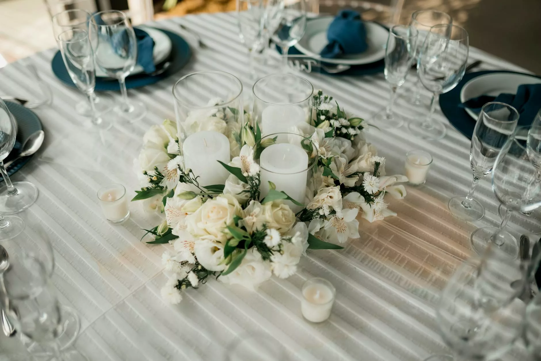 Centre de table mariage bougies : couronne de roses blanches autour de trois bougies piliers, dressage bleu