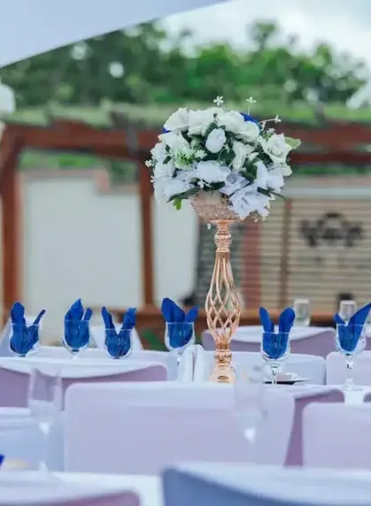 Table de mariage dressee en bleu marine avec serviettes nouees, fleurs blanches et chandeliers cuivres