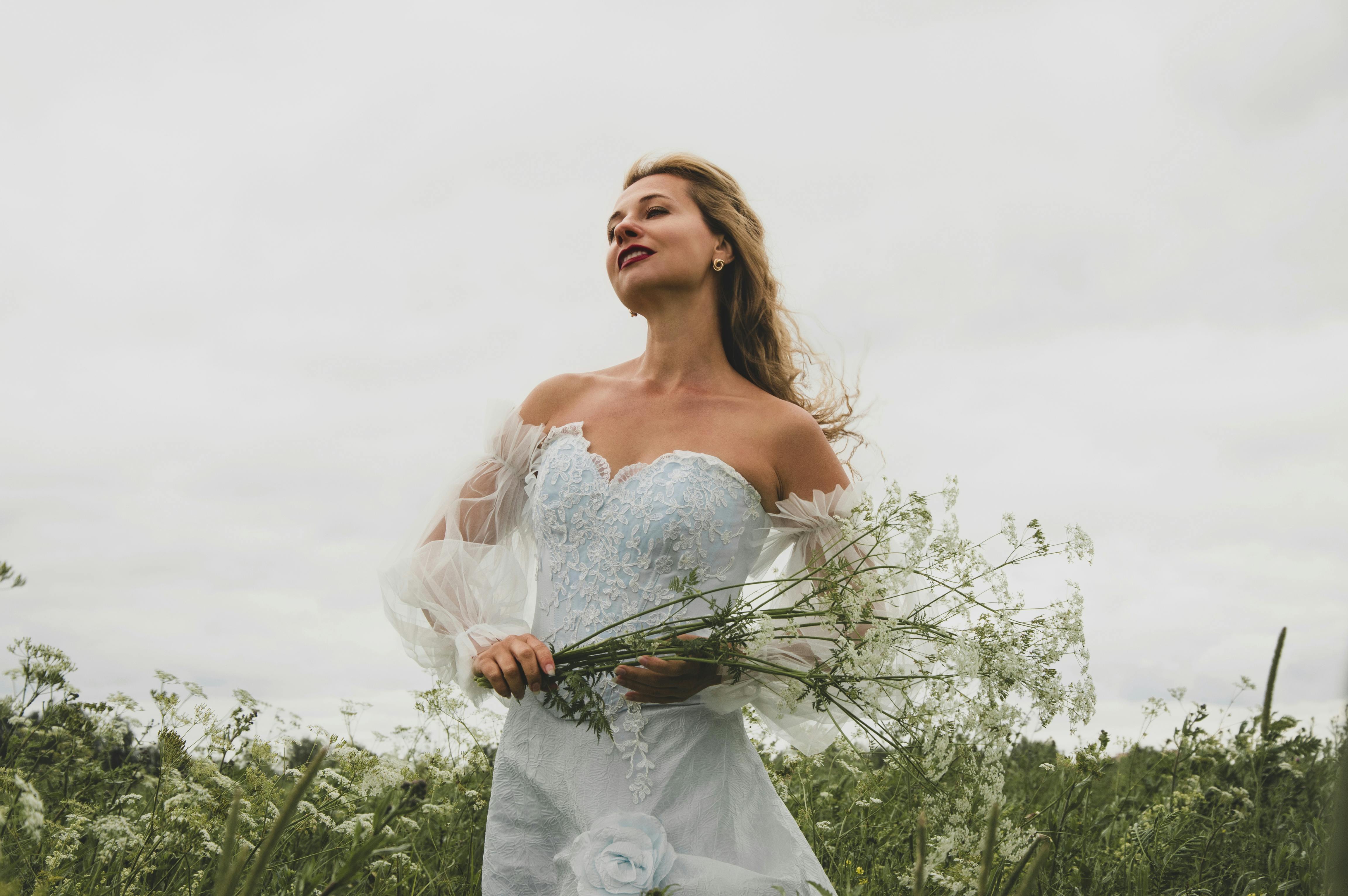 Mariée en robe blanche tenant un bouquet de fleurs sauvages blanches dans un champ