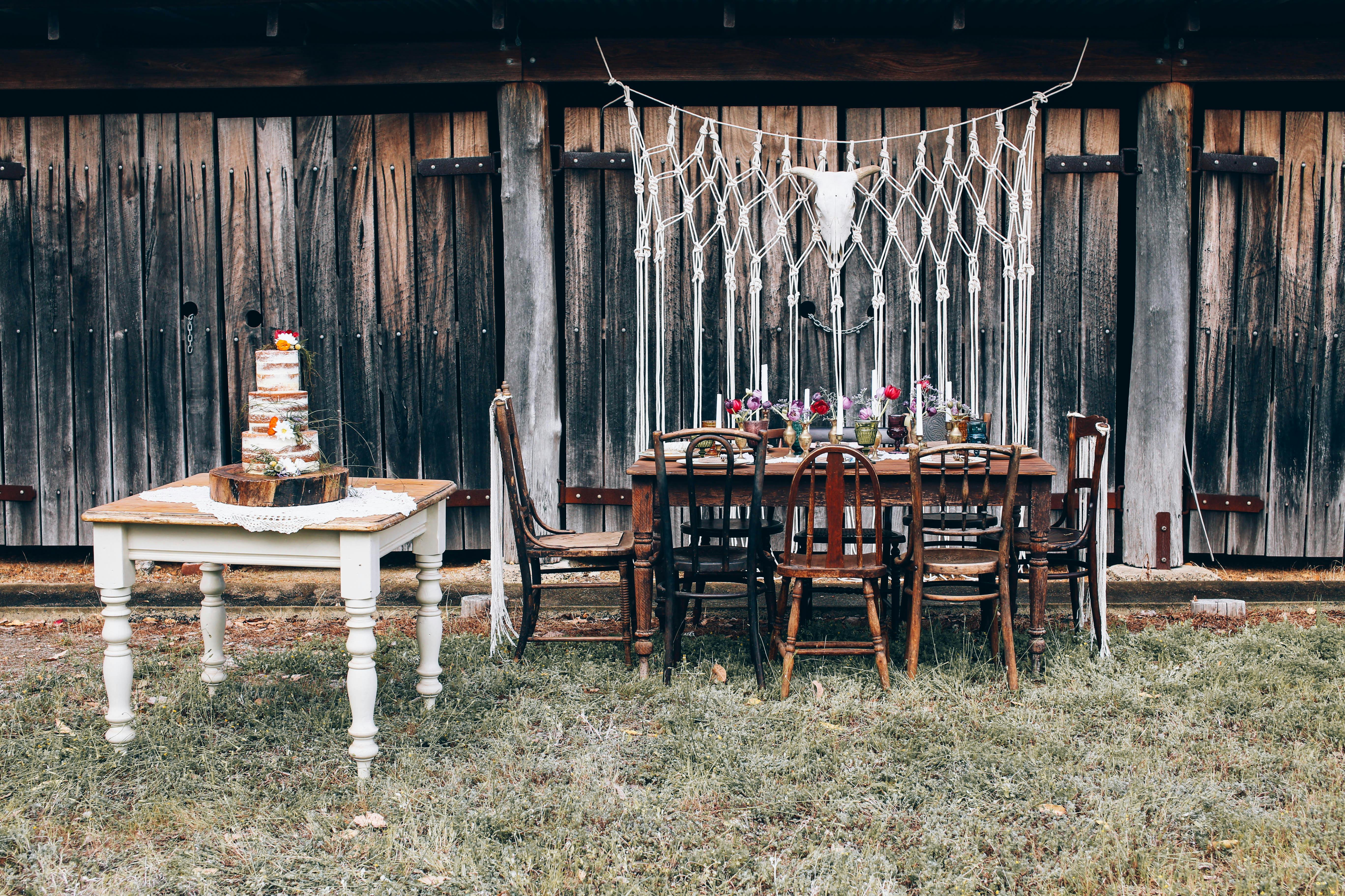 Coin lounge mariage champêtre avec chaises vintage en bois devant une grange