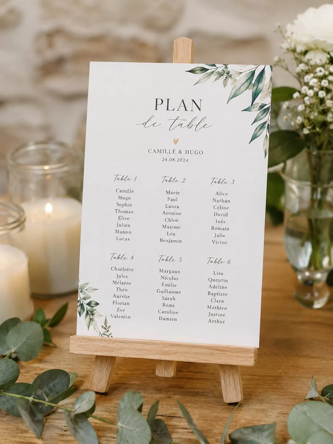 Petit chevalet en bois portant un plan de table de mariage avec verdure et bougies