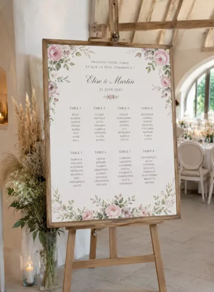 Grand chevalet en bois portant un plan de table de mariage fleuri dans une salle de réception
