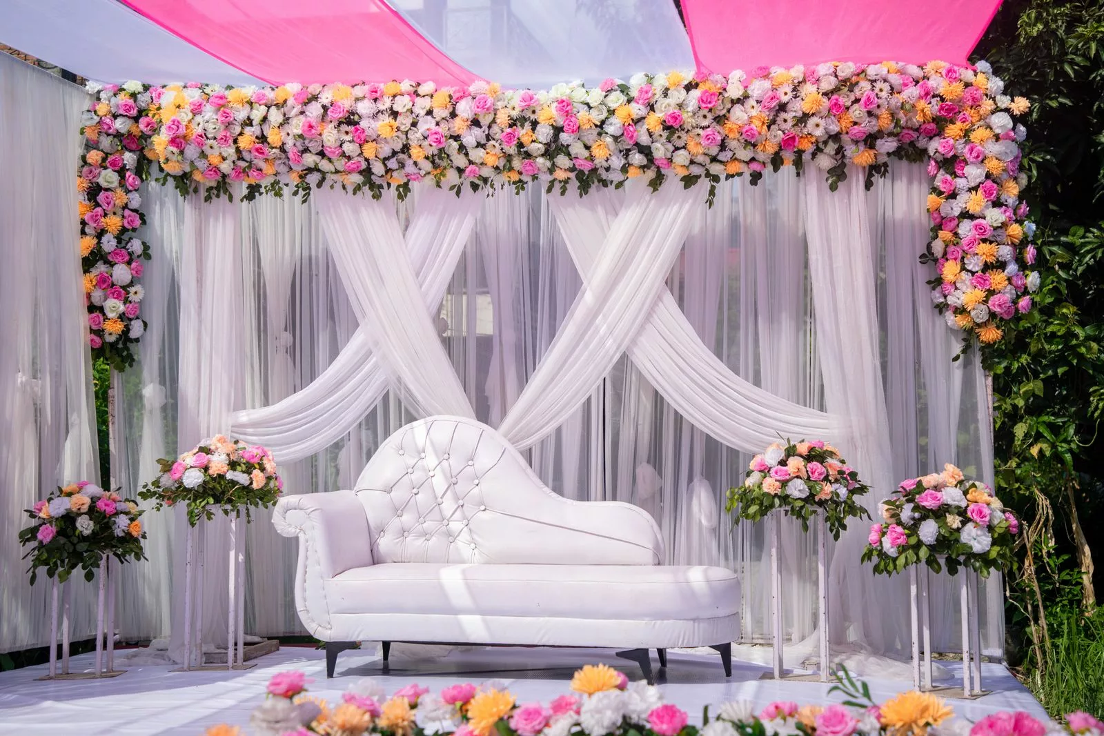 Arche florale de mariage pastel avec roses roses, pêche et blanches sur drapé blanc