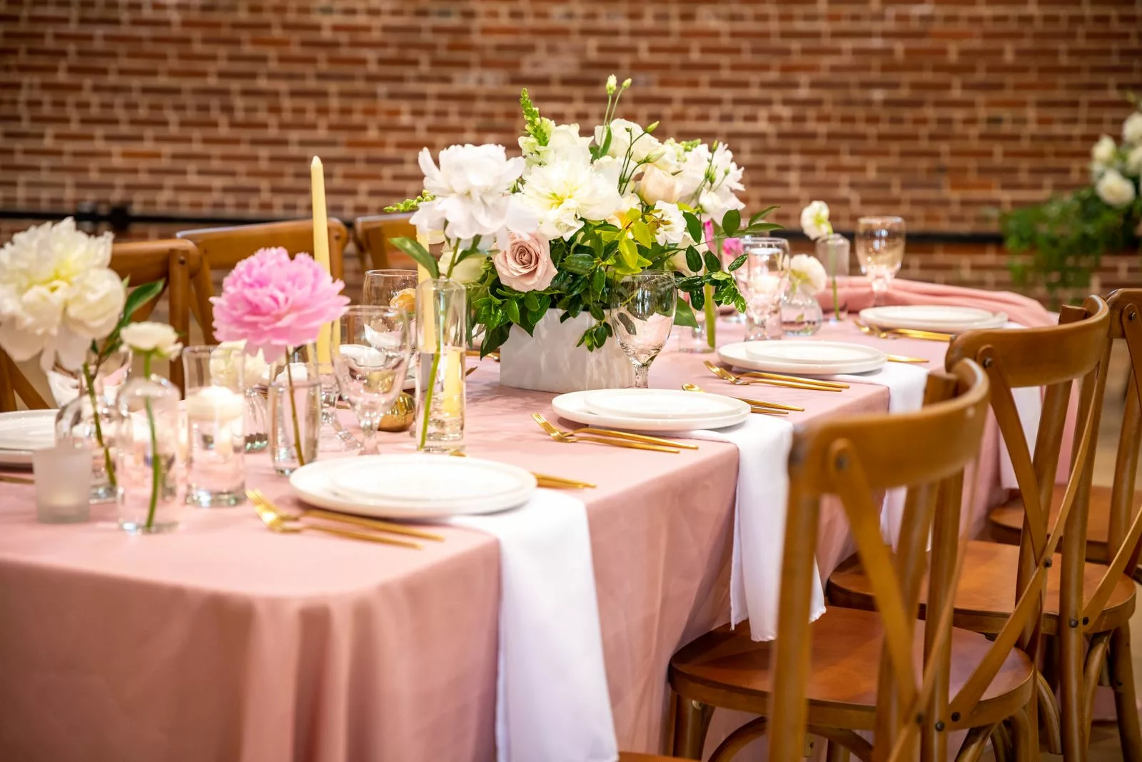 Table de mariage pastel avec nappe rose poudré, couverts dorés et pivoines blanches