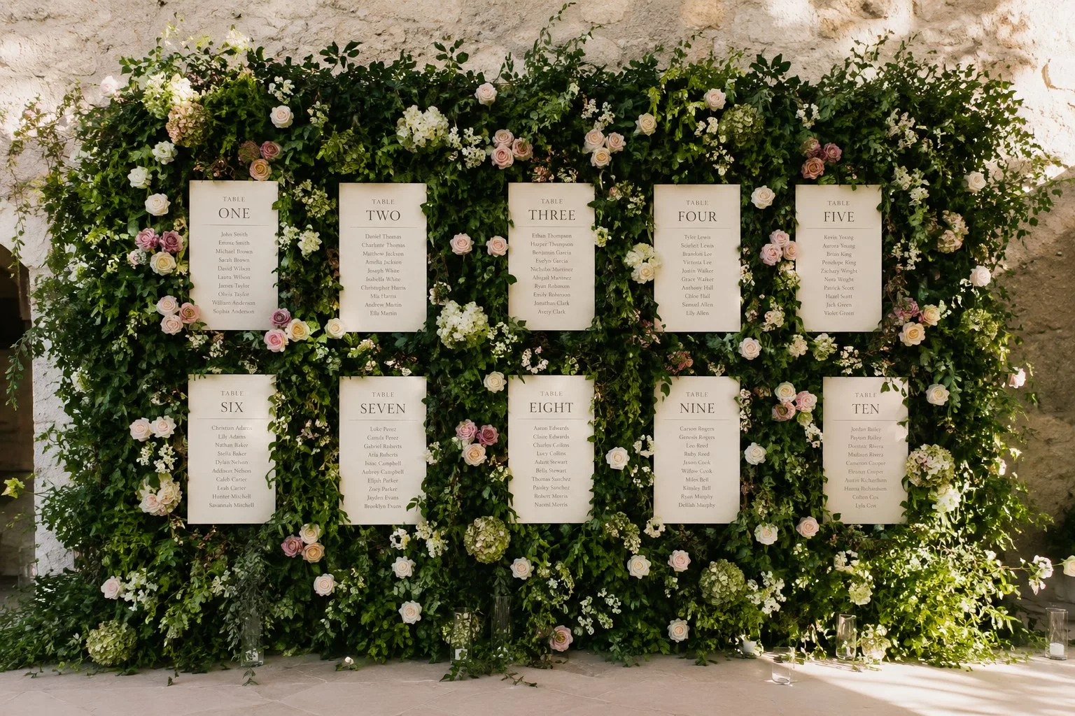 Plan de table de mariage sur un grand mur végétal fleuri avec roses et noms des tables