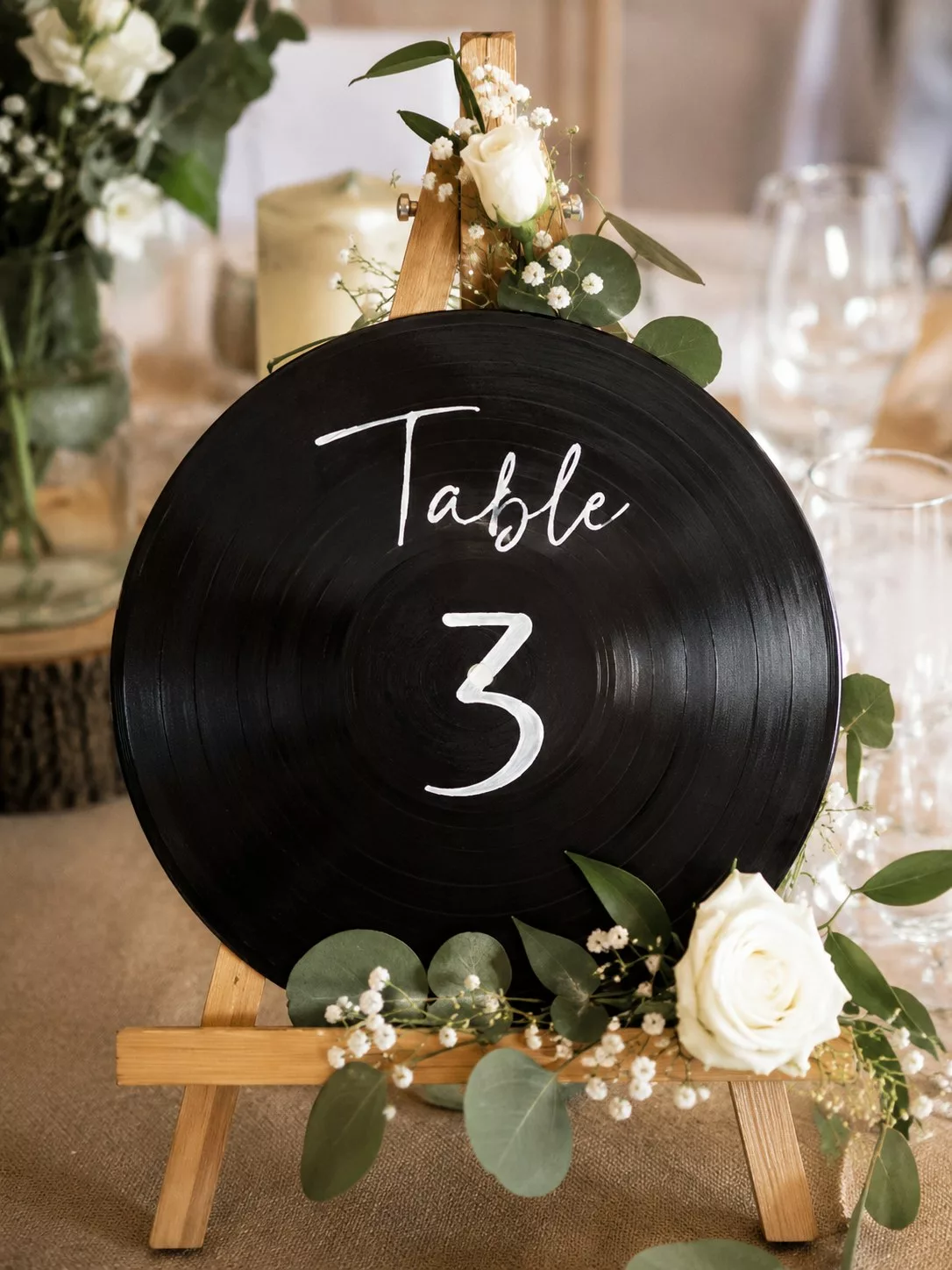 Disque vinyle peint au nom d'une table posé sur un chevalet fleuri, DIY mariage musique