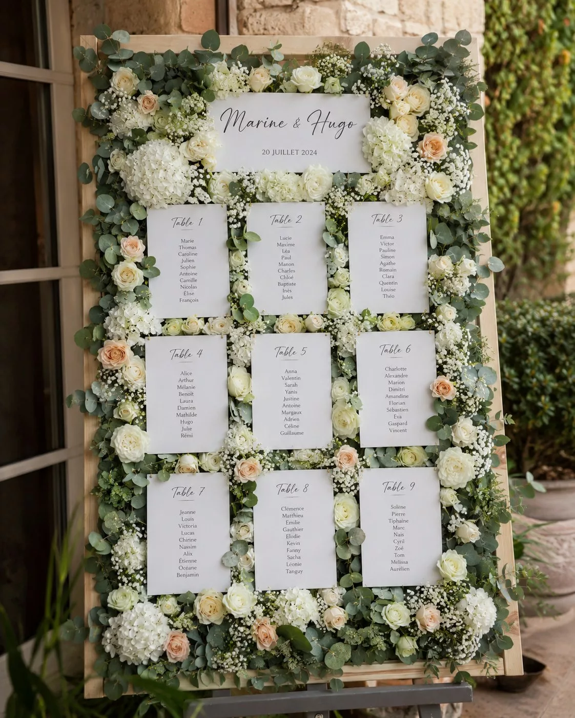 Plan de table de mariage sur un panneau encadré de fleurs blanches et d'eucalyptus