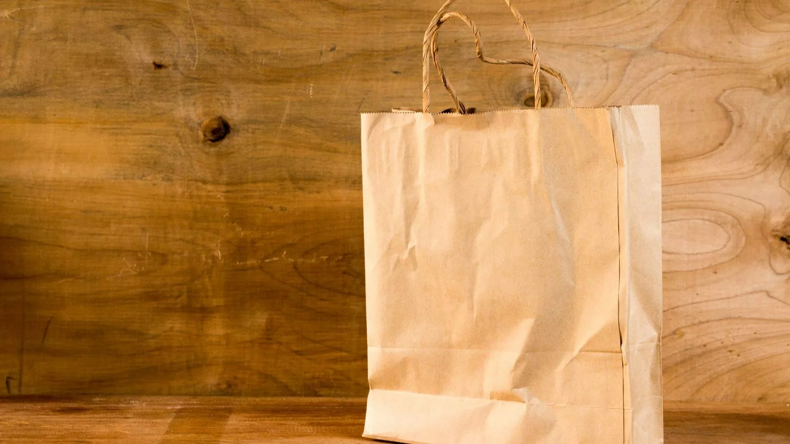 Sac en papier kraft fini avec anses en ficelle, posé sur une table en bois