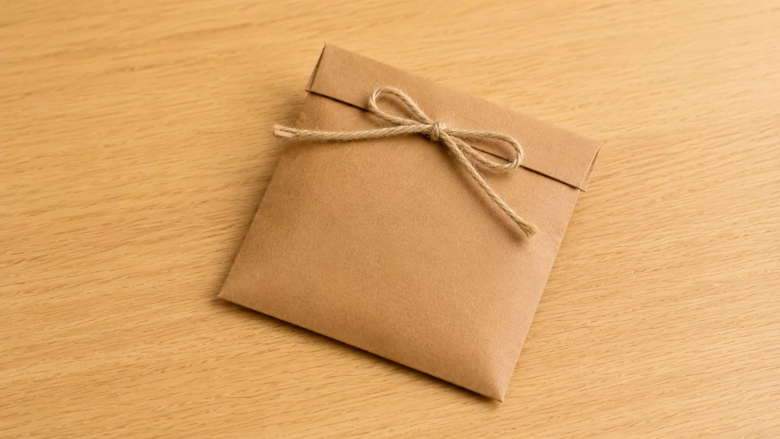Sachet cadeau plat en papier kraft brun, fermé par un nœud de cordelette en jute