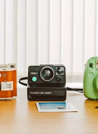 Trois appareils photo instantanés sur une table en bois, avec leurs tirages éparpillés