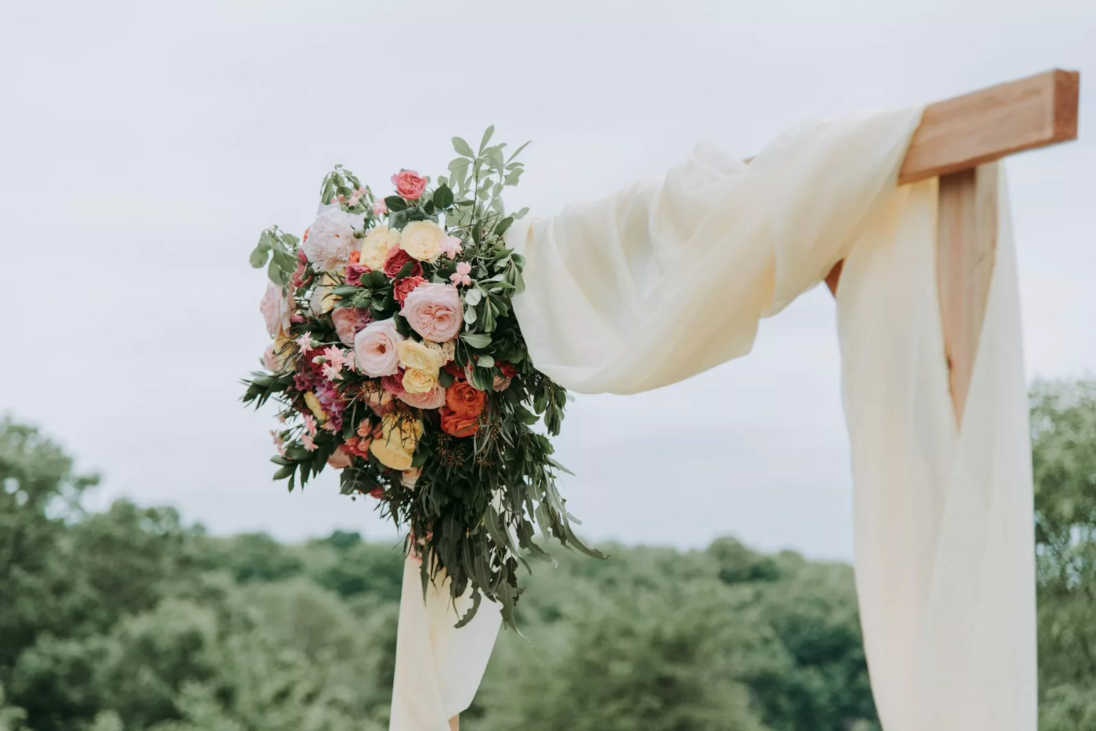 Arche florale avec voilage crème et bouquet de roses colorées, en extérieur