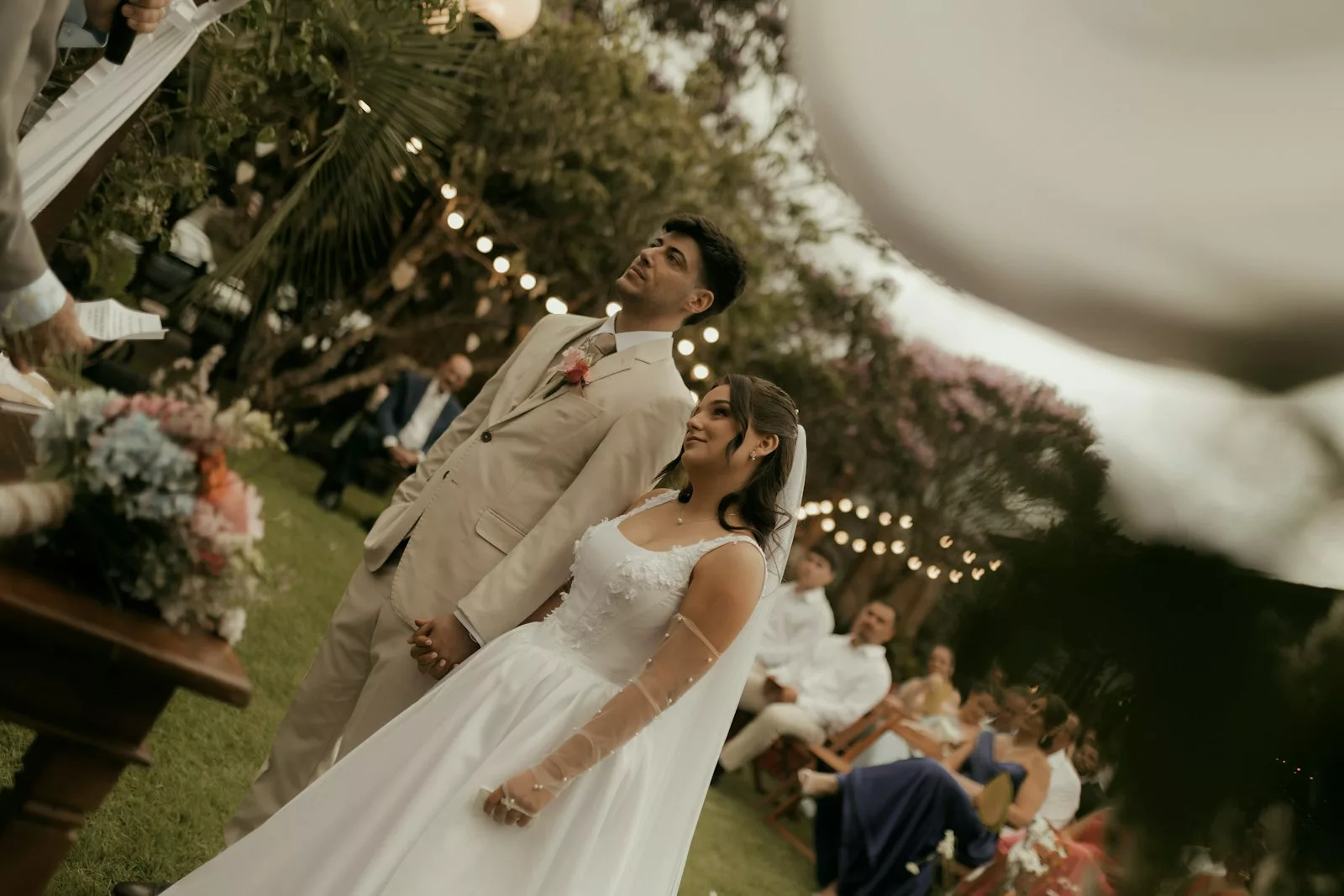 Couple face à l'officiant lors d'une cérémonie laïque en extérieur avec guirlandes lumineuses