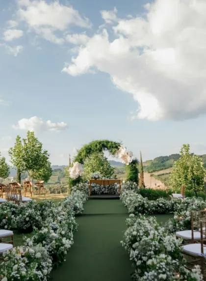 Cérémonie laïque en extérieur avec allée florale et arche végétale devant un paysage de collines