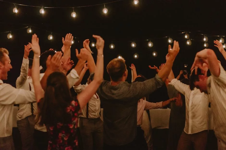 Invités les bras en l'air sur la piste de danse d'un mariage sous des guirlandes lumineuses