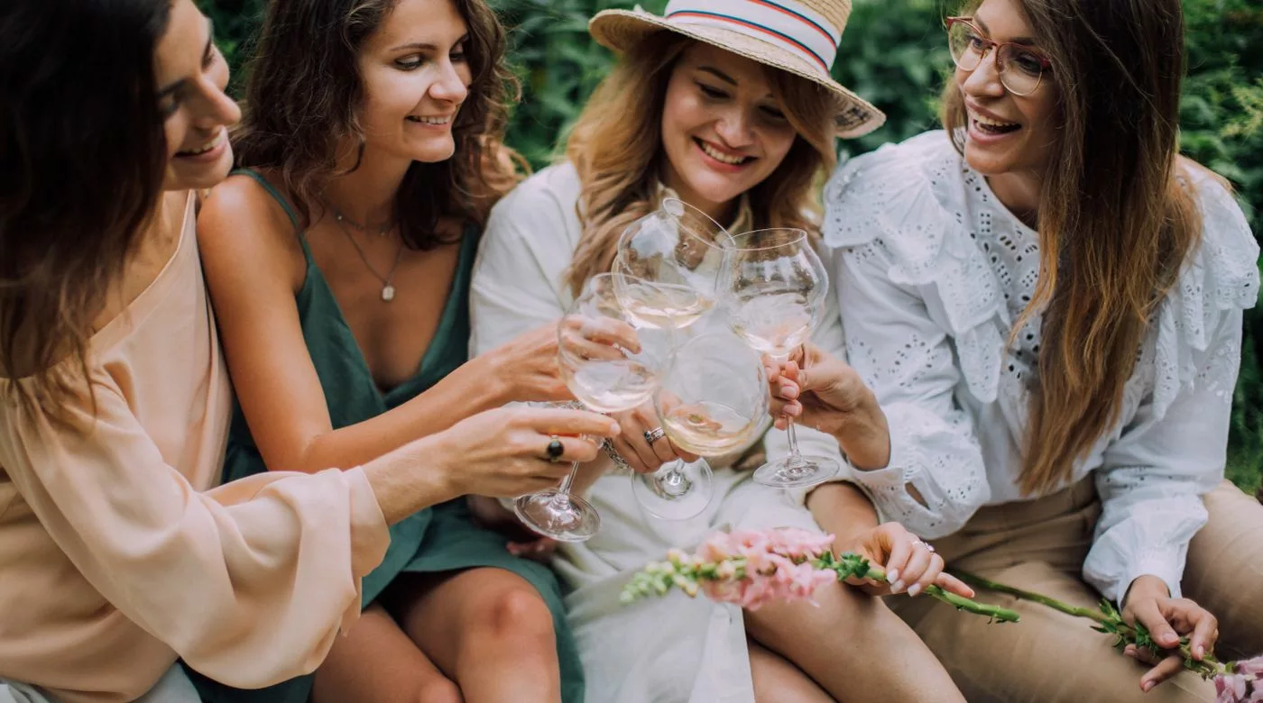 EVJF pas cher : quatre amies trinquent avec du vin blanc lors d'un pique-nique champêtre