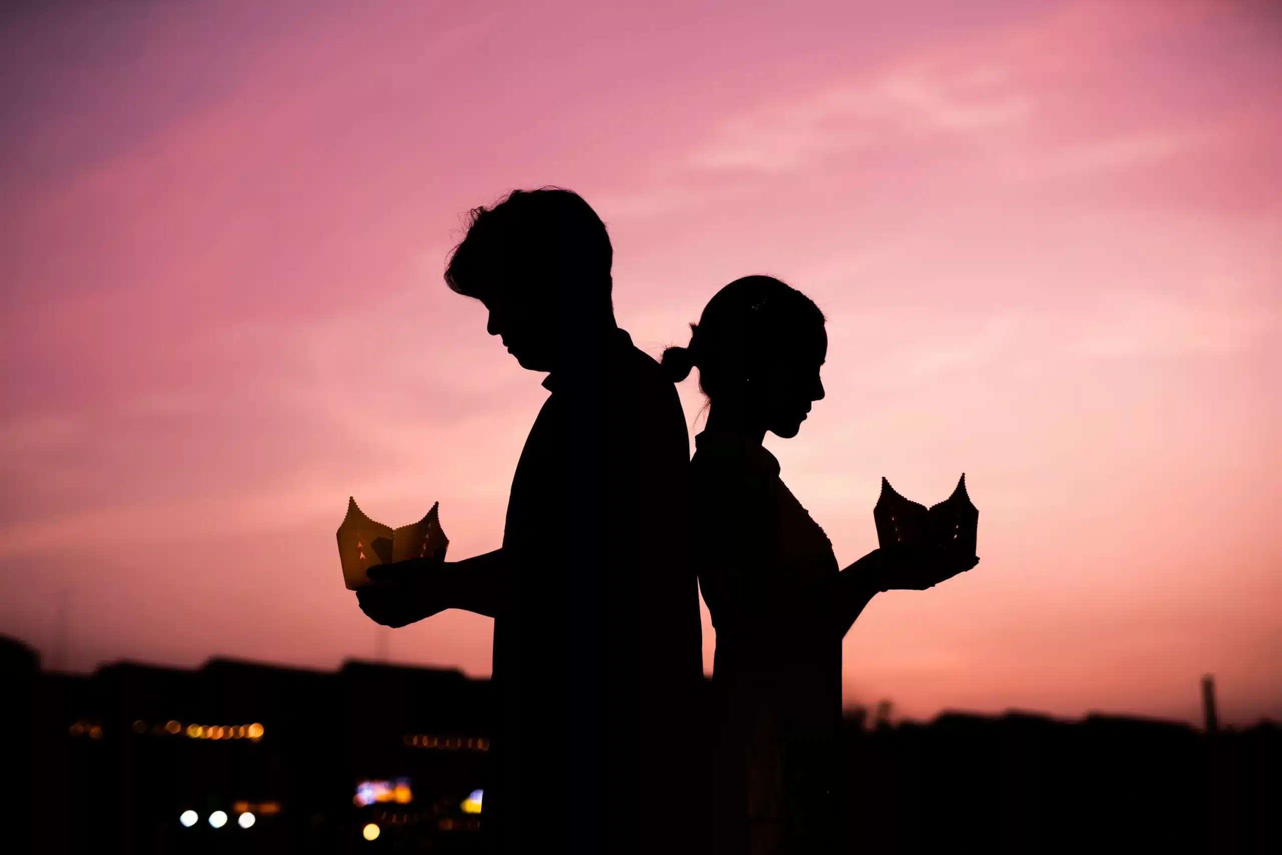 Silhouette de mariés tenant des lanternes en papier au coucher de soleil