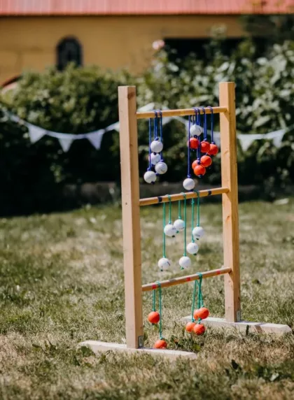 Olympiades de mariage : jeu de lancer d'echelle en bois installe dans un jardin decore de fanions blancs