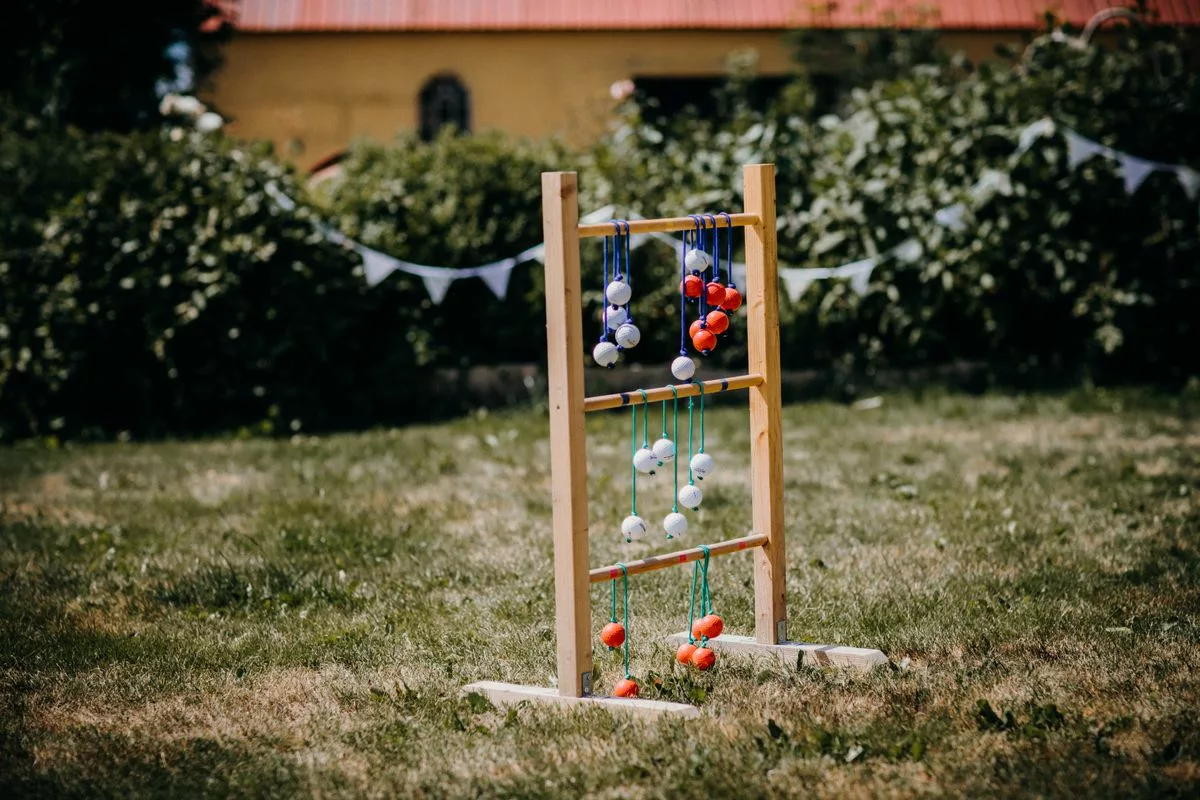 Olympiades de mariage : jeu de lancer d'echelle en bois installe dans un jardin decore de fanions blancs