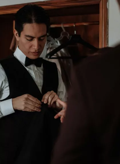 Marié en chemise blanche ajustant son gilet noir et son nœud papillon avant la cérémonie