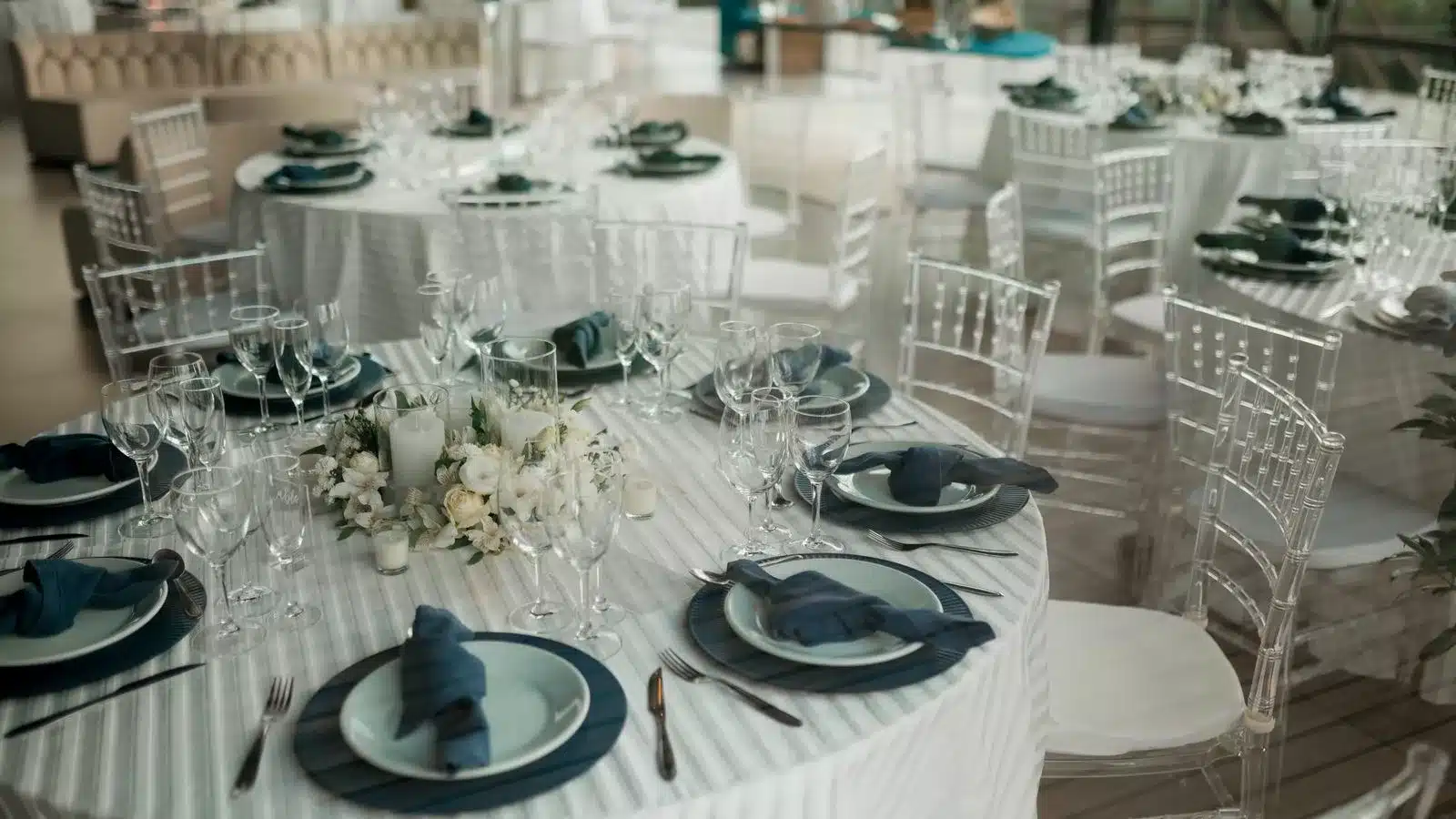 Tables rondes dressées pour 150 invités avec décoration florale blanche et serviettes bleu marine