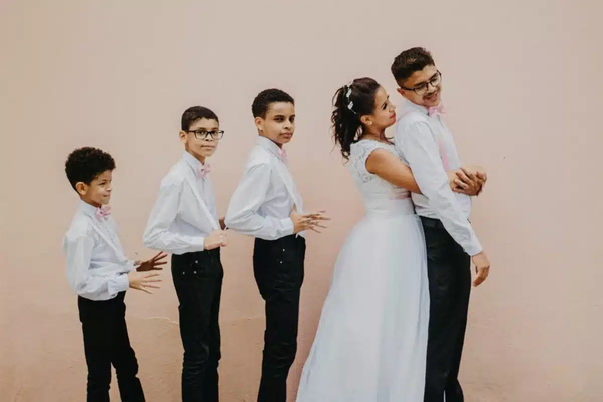 Portrait de maries avec plusieurs enfants d honneur alignes contre un mur rose