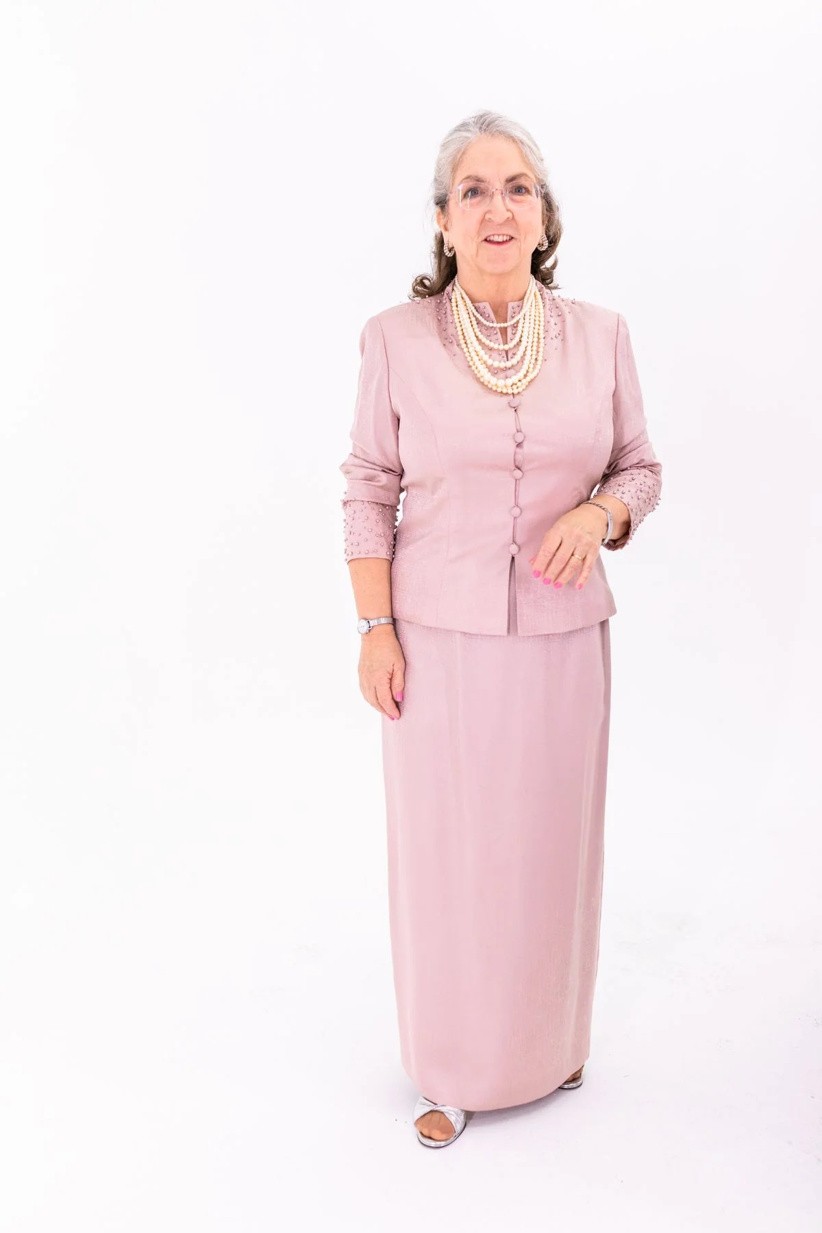 Invitée 70 ans en ensemble jupe midi et blouse rose cendré avec collier de perles
